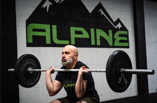 Alpine CrossFit member performing a front squat in front of the Alpine mountain wall mural